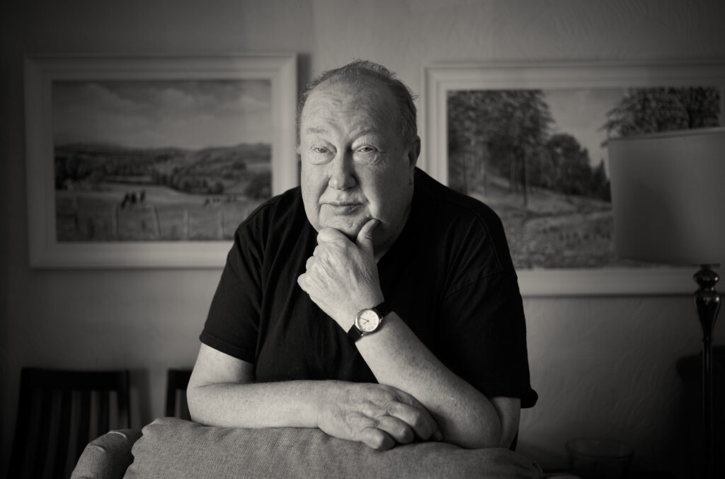 Artist Rob Lees, poses for a portrait in his living room, two of his painting are behind him.